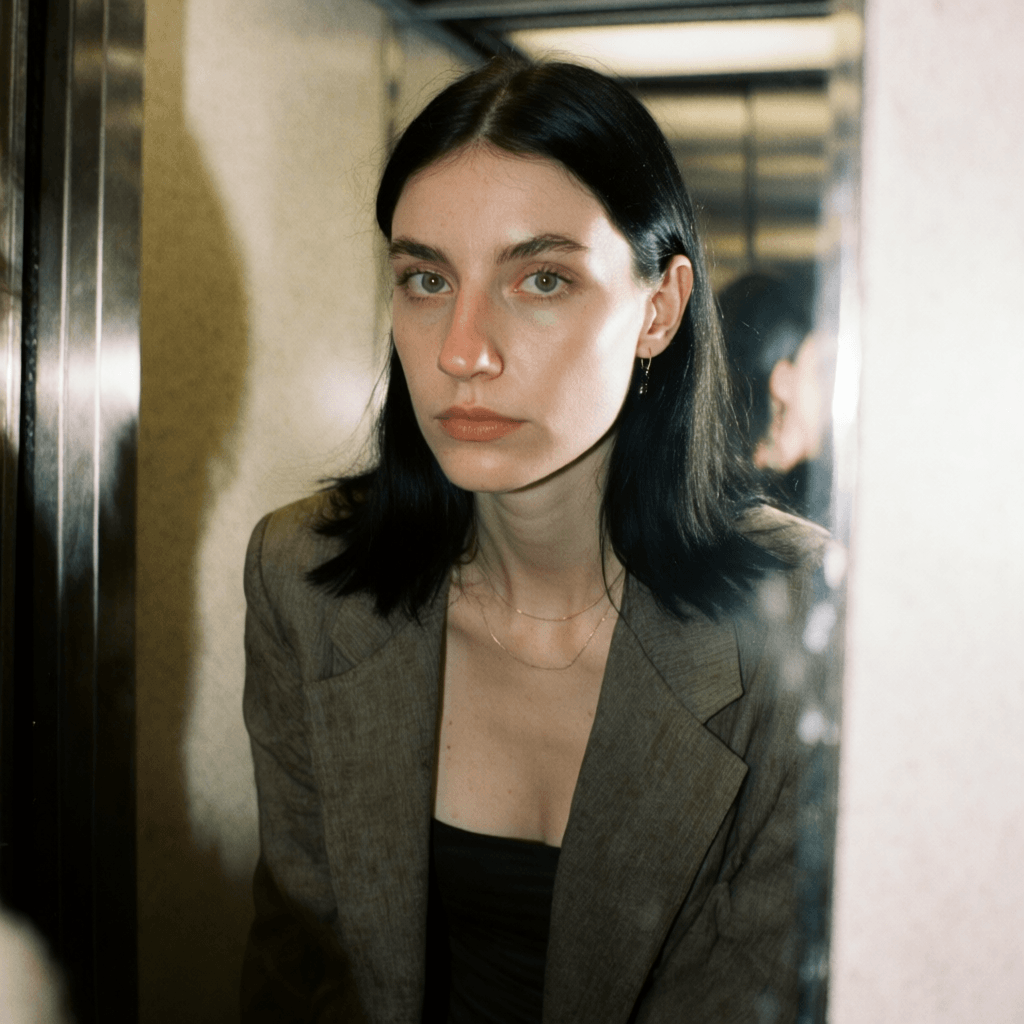 Emma-Jane MacKinnon-Lee — mirror self portrait, straight black hair tucked behind the ear